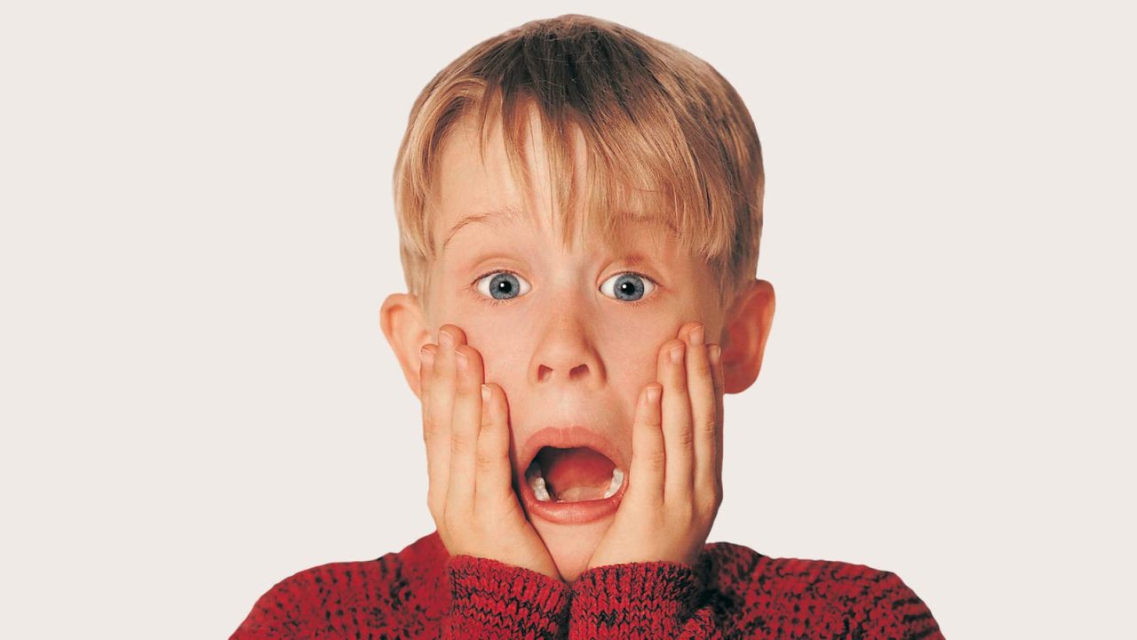 Снимка на малкия Маколи Кълкин от коледната комедия "Сам вкъщи", на която той е облечен с червен пуловер, хванал е лицето си ръце и гледа учудено.